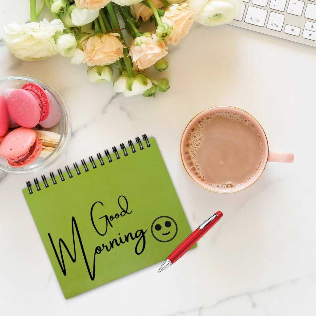 A beautiful close-up of a pink rose bud on a dark textured background, featuring three cute pink hearts hanging from a golden line in the upper right corner and elegant white script font reading Good Morning.