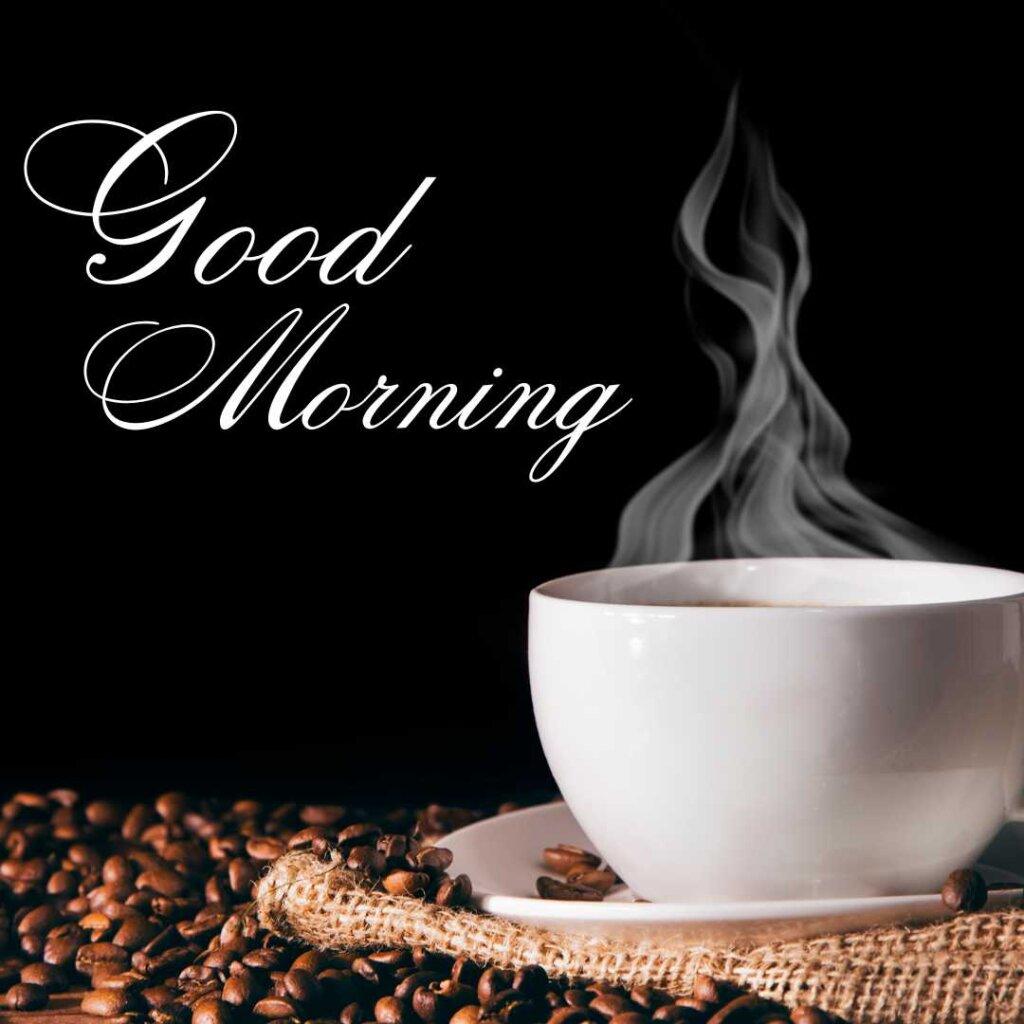 Steaming white coffee cup and roasted coffee beans against a black background with Good Morning text.