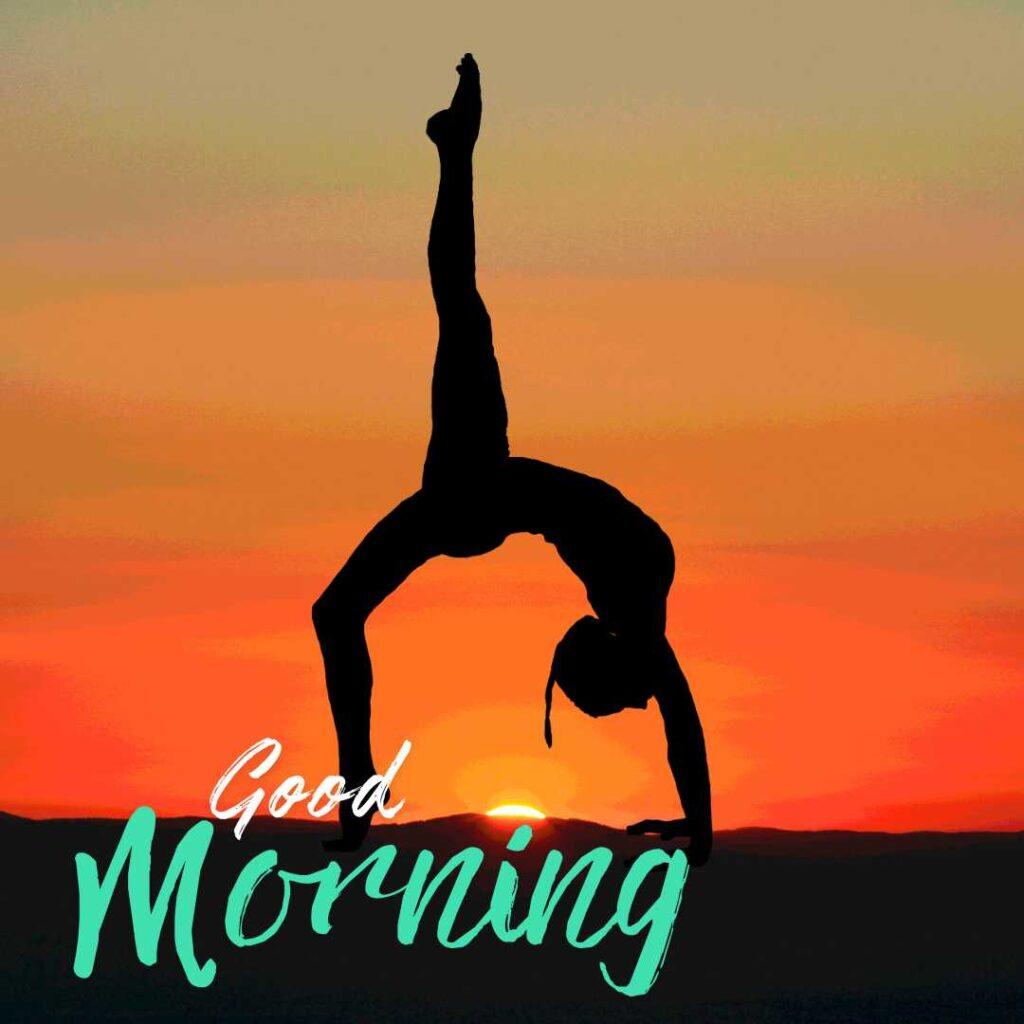 A black silhouette of a person doing a one-legged wheel pose or handstand inversion against a vibrant orange sunset with Good Morning text.